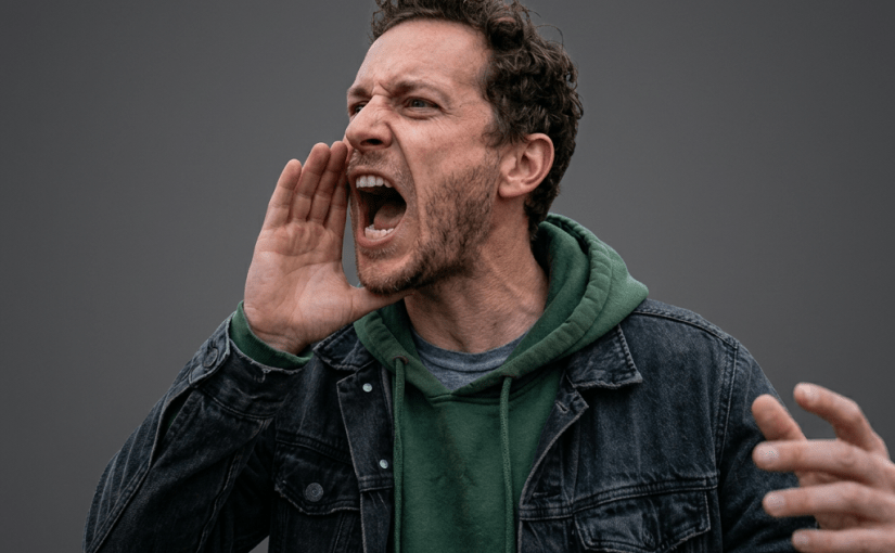 Man in green hoodie and black jacket shouting with hand near mouth